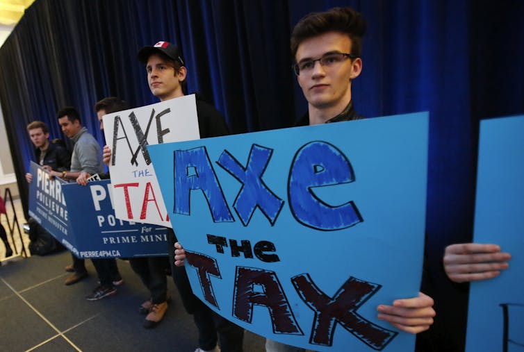 A row of people are seen holding signs against a blue curtain.