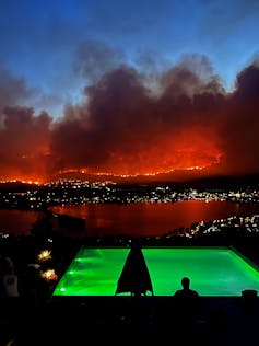 A man stands by a pool looking out over a wildfire