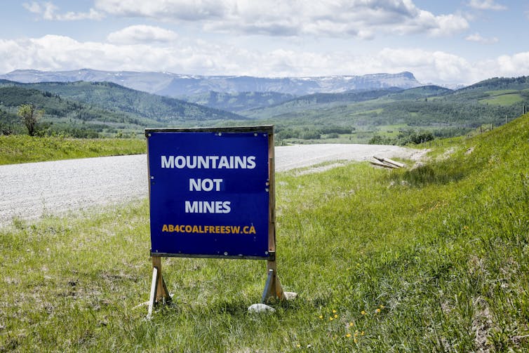 A sign on the grassy shoulder of a highway reads Mountains Not Mines.