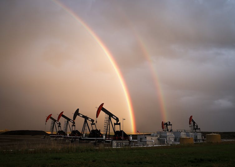 Rainbows and orange light behind a row of pumpjacks.
