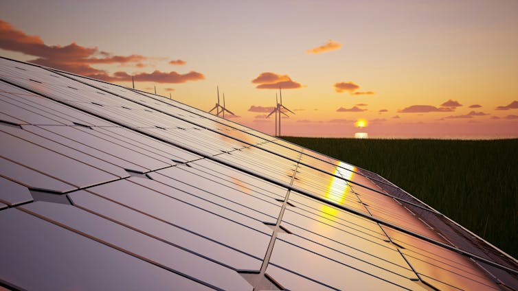 a solar panel with wind turbines in the far distance with the setting sun